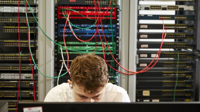 Student working on a computer with networking equipment in the background