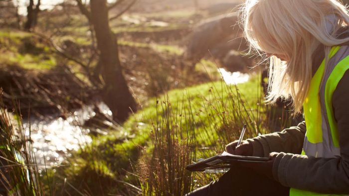 A student sat by a small stream, writing in a notebook