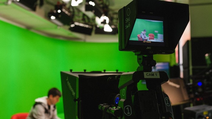 A tv studio camera filming a student sat in front of a green screen