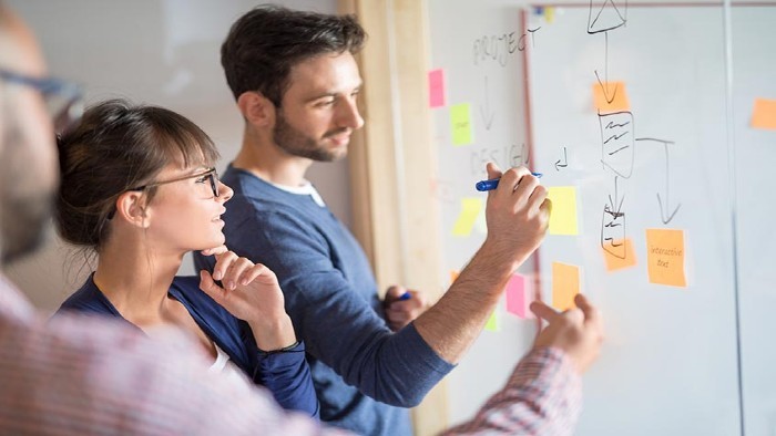 Three people stood writing on a whiteboard with pens and sticky notes