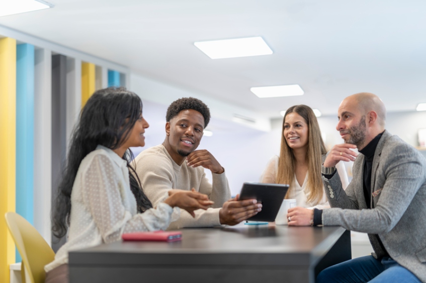 A group of professionals conversing around a table in a brightly lit office space