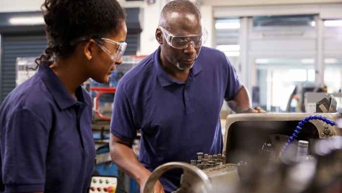 A man wearing goggles is showing an apprentice how to operate a piece of equipment