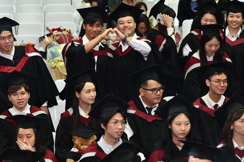 Students sat in bleacher dressed in graduation gowns and celebrating