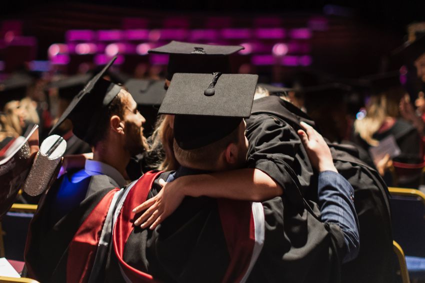 Students hugging at ceremony wearing graduation gowns