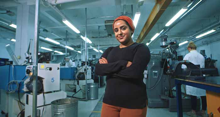 Confident young woman standing in front of equipment in an engineering lab. She has her arms folded and a smile on her face.