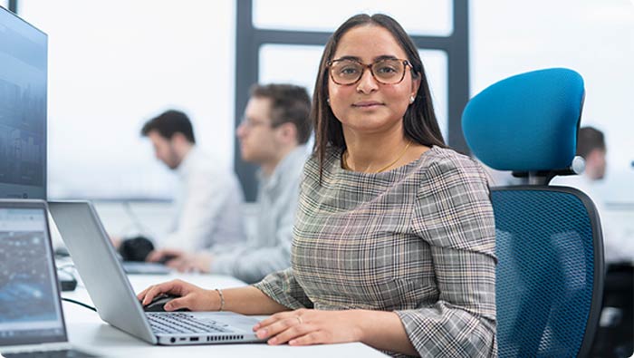 A young employee sitting at a laptop, with several colleagues in the background