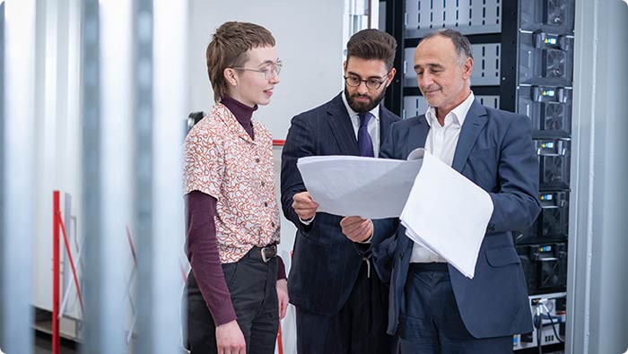 Three people talking and reviewing a document with computing equipment in the background