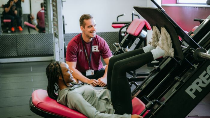 student in a leg machine with personal trainer