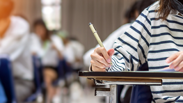 Students in an exam room, working individually at their own desks.