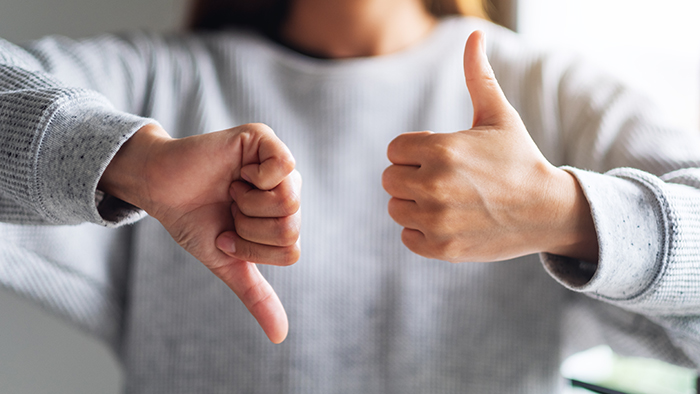 Someone facing the camera, holding one hand in a thumbs-up gesture and one in a thumbs-down. 