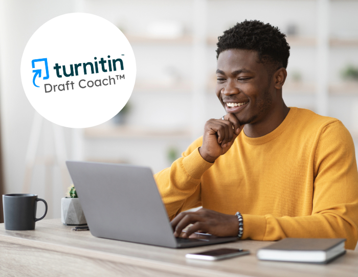 A black male student in a bright yellow jumper looks at his laptop smiling.