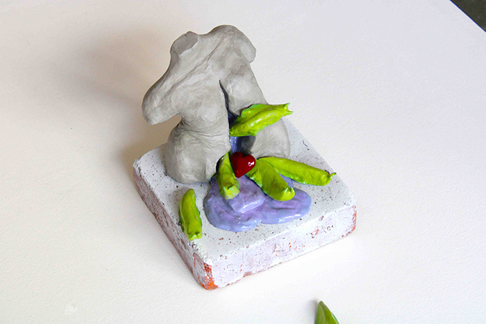 A clay statue of a grey torso, with green slugs emerging from within.