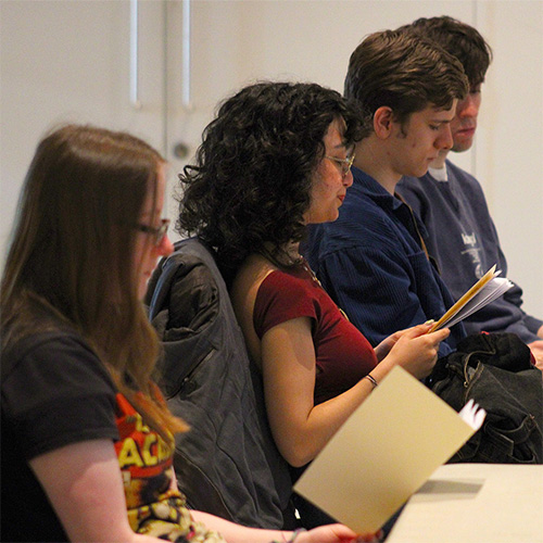 A group of students seated in a row, reading copies of a zine produced to accompany the event they are attending.