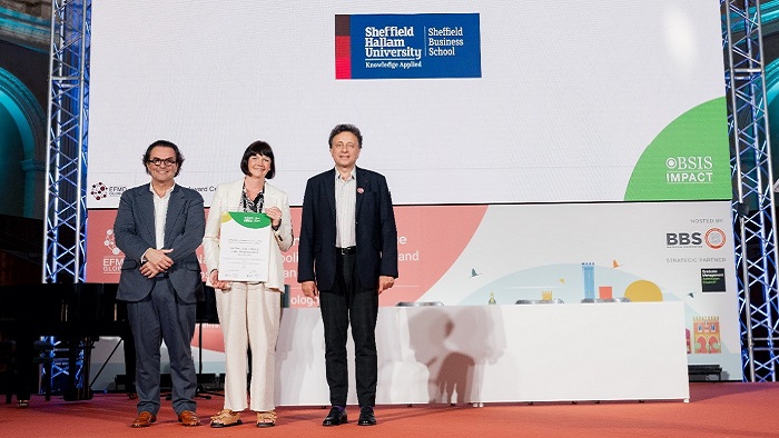 Three people in business clothes holding up a certificate on a stage