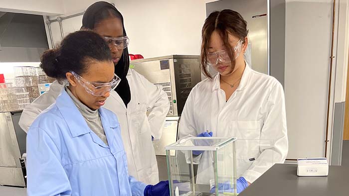 Three students in lab coats working with lab equipment 