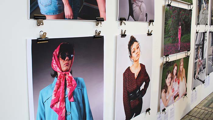 A white wall with large photographs exhibited on it. The photographs show models who have been style in clothes from St Luke's. 