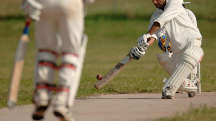 Men playing cricket on field wearing cricket whites