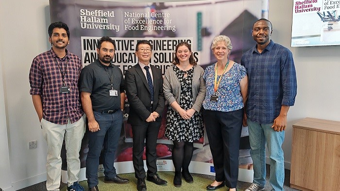 A group of six men and women in front of a large banner in an office