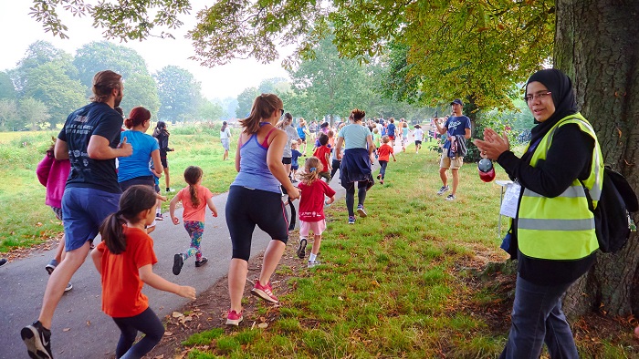 People running through a park being cheered on by a woman parkrun volunteer