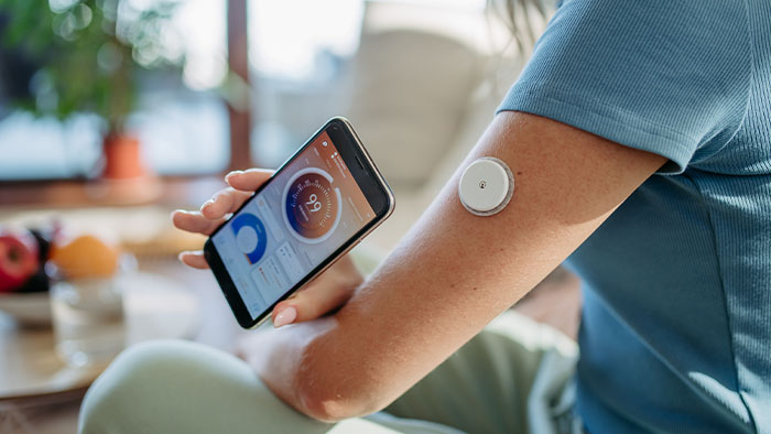 A person using their phone to read a glucose monitor on their arm