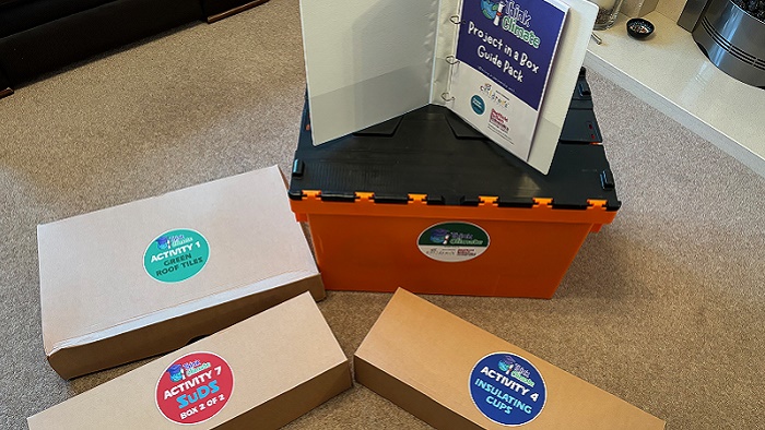 Three cardboard boxes on a carpet next to a bigger orange plastic box with an open booklet on top 