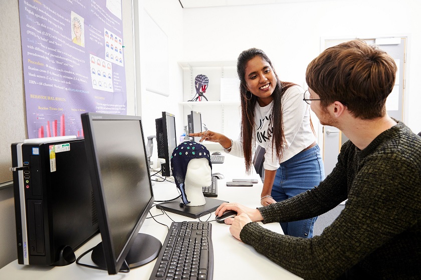 Two students sat at a desk with an EEG cap on the desk