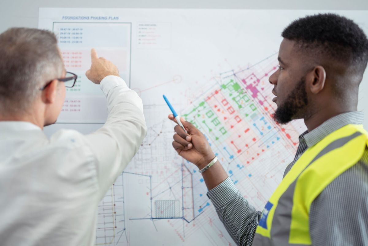 Two people reviewing construction plans which are displayed on the wall.