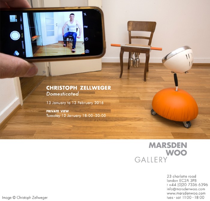 Flyer for the Domesticated gallery. A person is getting their picture taken on a mobile phone. Next to him is a wooden chair with a bar on top and pieces of metal under the seat and cream and orange lamp on wheels