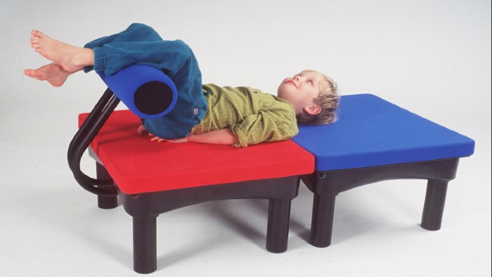 Toddler lying on red and blue platforms with his legs up, supported by a padded tube