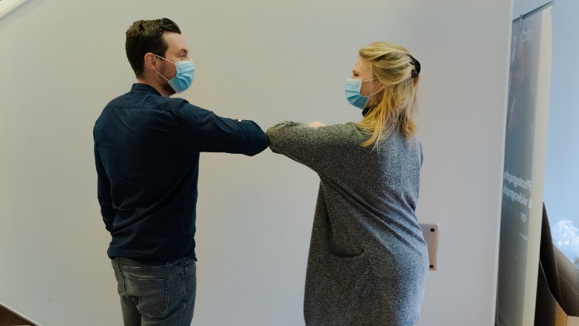 Two people wearing face masks bumping elbows
