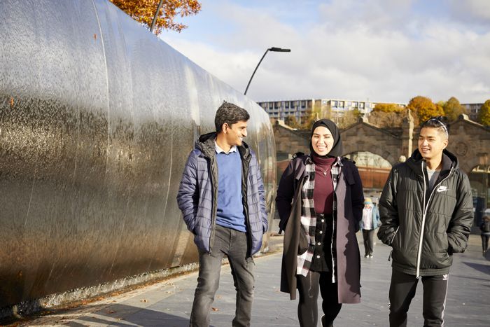 Two men and a woman from different ethnic backgrounds walking through Sheffield, smiling. 