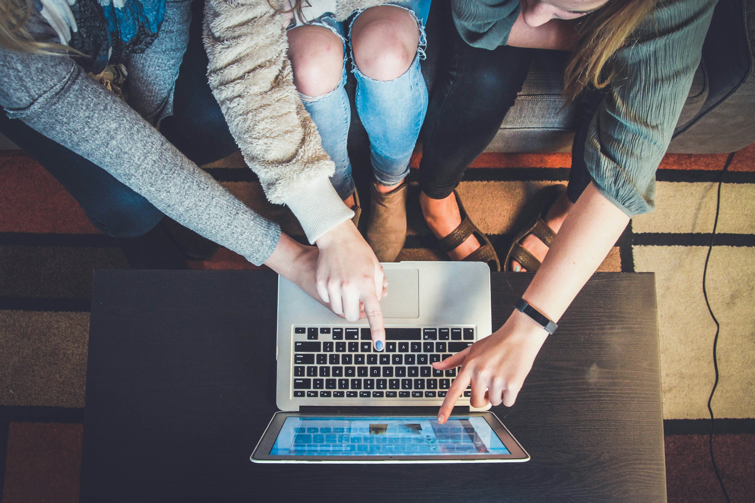 Three people pointing at silver laptop