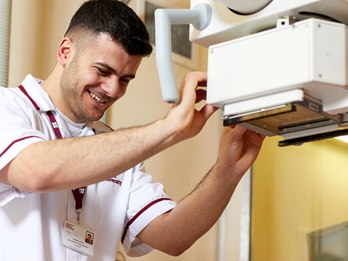 Male diagnostic radiographer working machine while smiling.