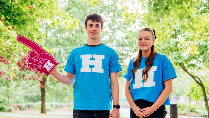 Two student ambassadors are wearing blue t-shirts at an open day, with trees in the background.